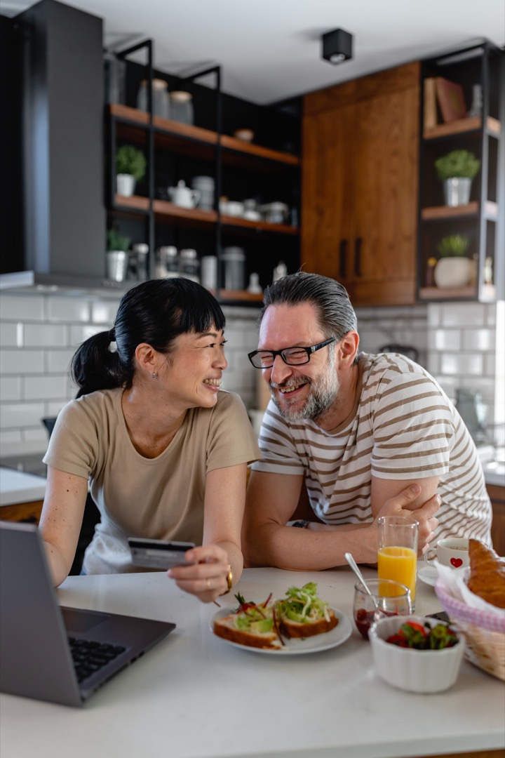 Cheerful couple looking at laptop screen in kitchen during breakfast