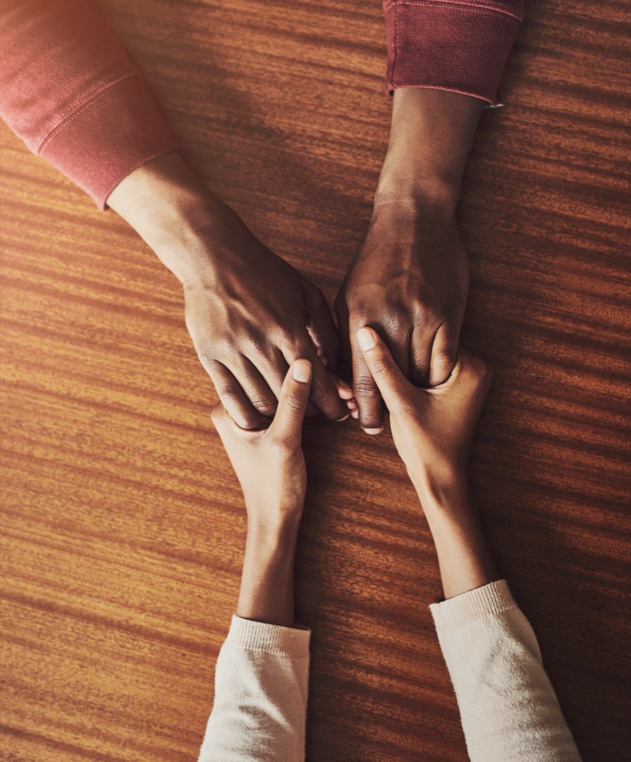 Couple, holding hands and above for support in home for care, connection and empathy for mental health. People, comfort and partner for help with kindness, bonding and solidarity for grief on table.